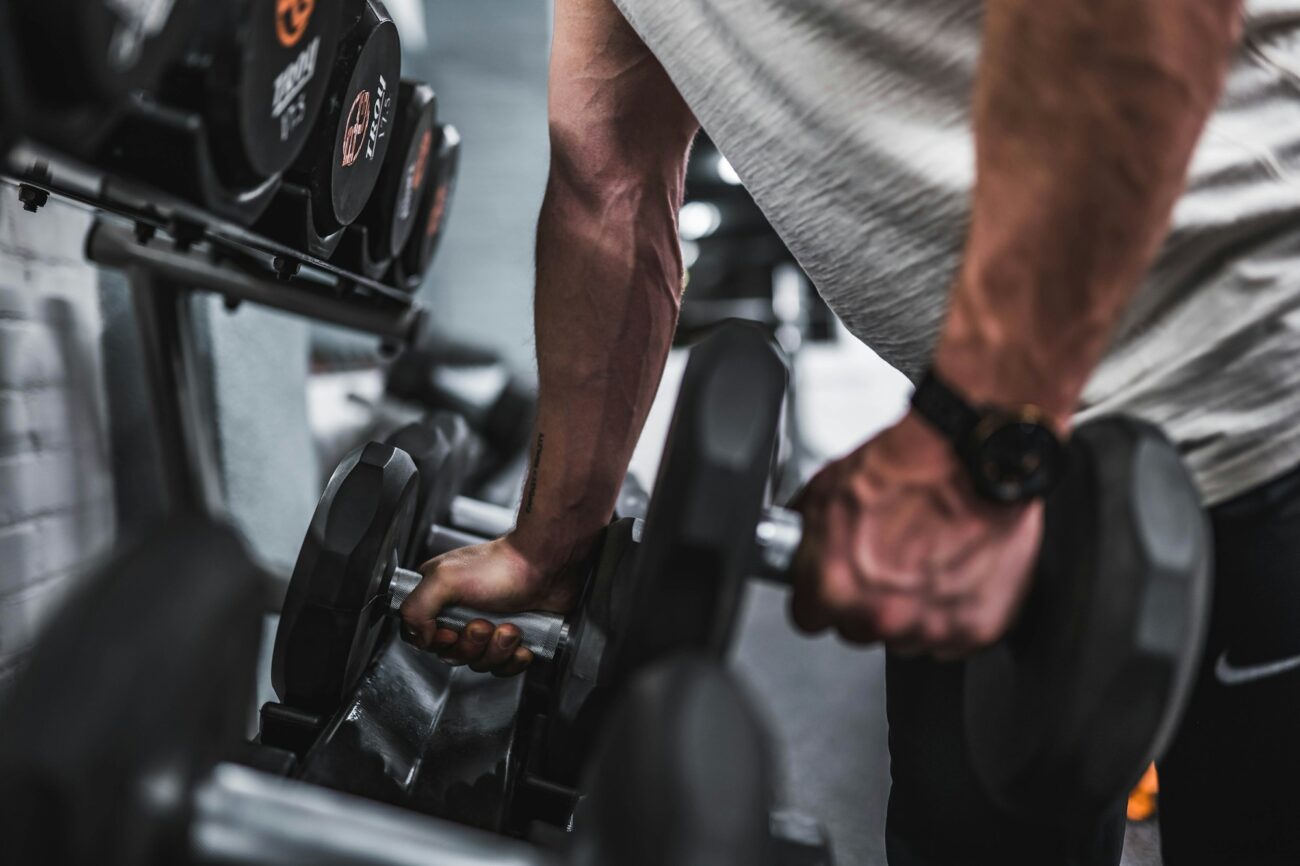 A man gripping two heavy dumbbells as he lifts them off a gym rack