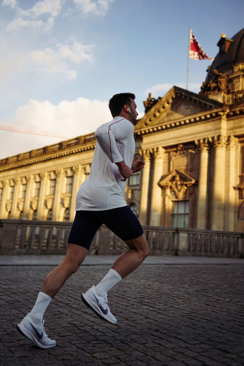 A man running along a cobbled street past a large old building on a sunny evening