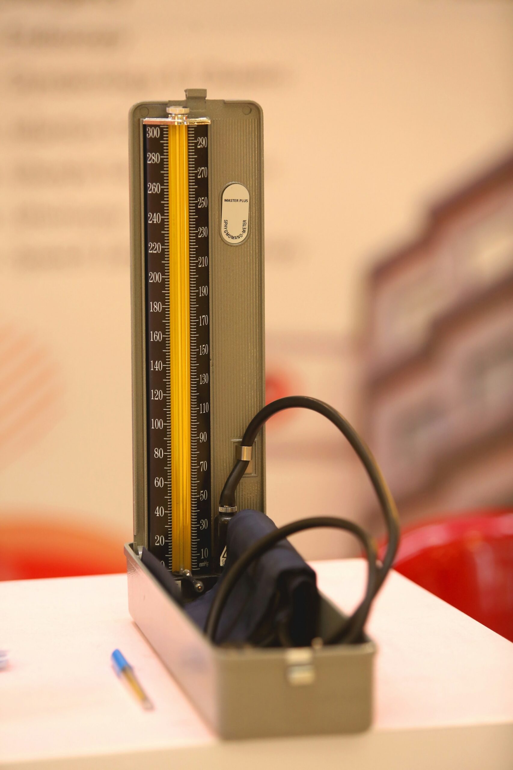 An old-style column blood pressure gauge with its upper-arm cuff and rubber tubing folded into an open metal case