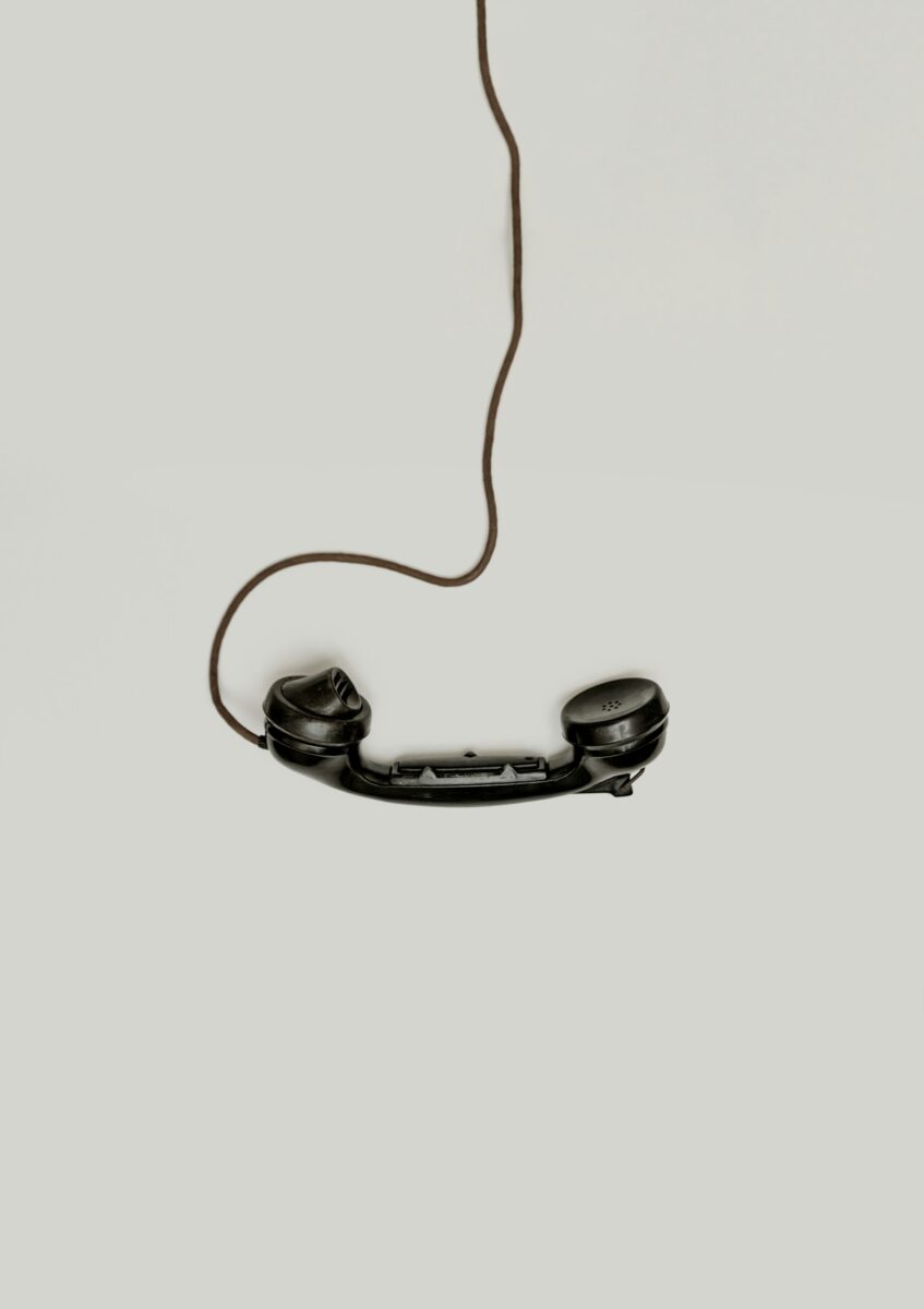 An old black telephone handset hanging on its curly cord against a plain light wall