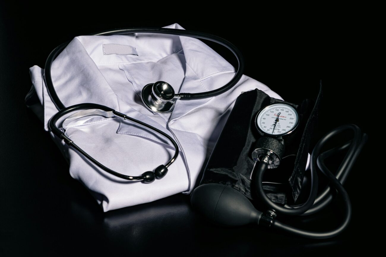 A manual blood pressure cuff with its dial gauge and bulb lying beside a stethoscope on a folded white coat
