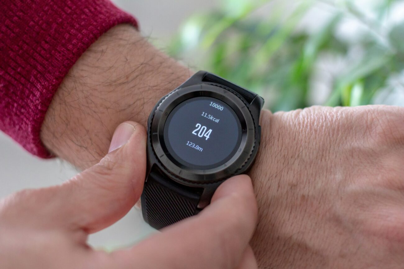 A round black smartwatch on a wrist showing steps, a kcal figure and distance on its screen