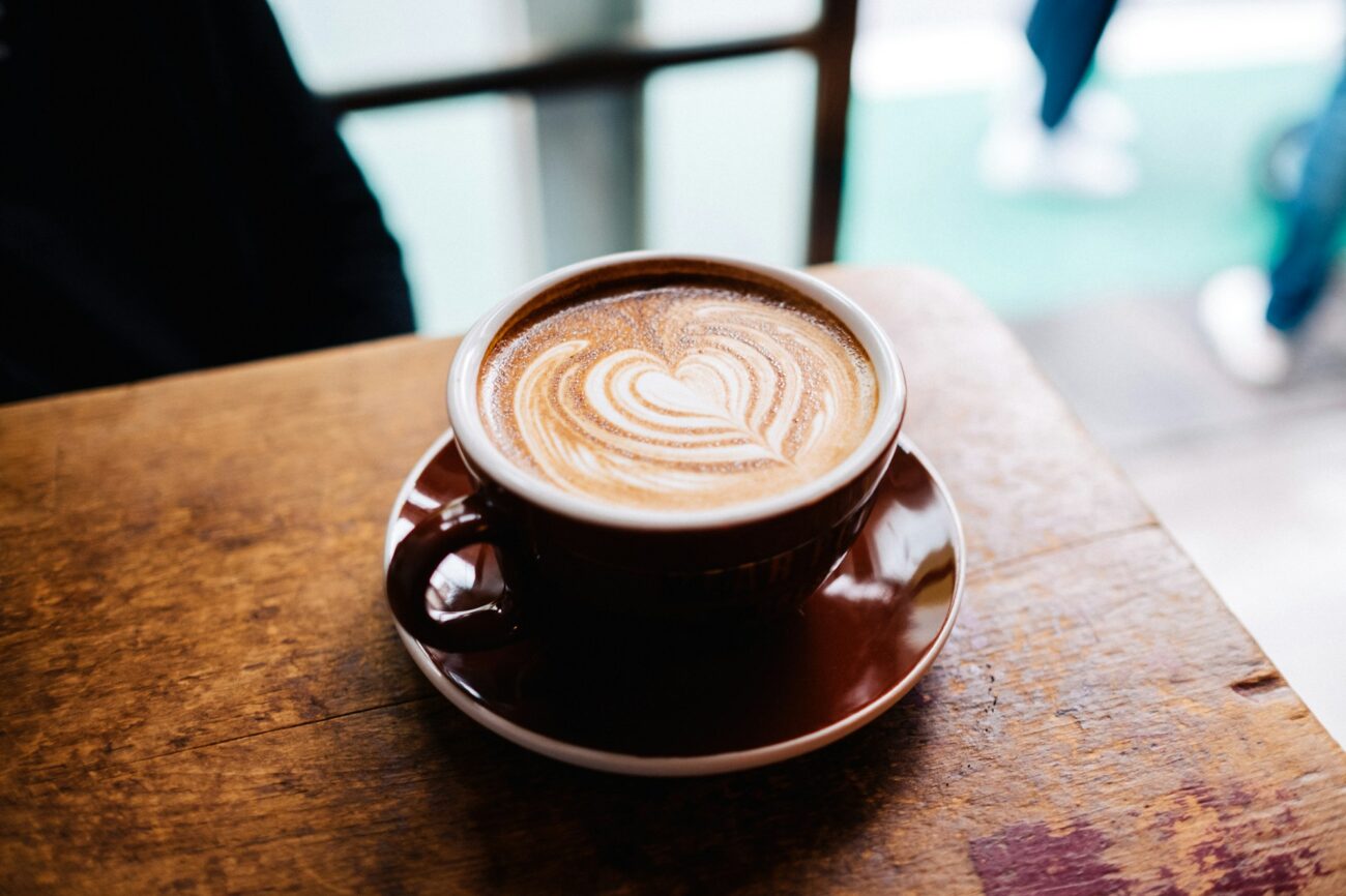 A cup of coffee with heart latte art on a saucer on a wooden cafe table