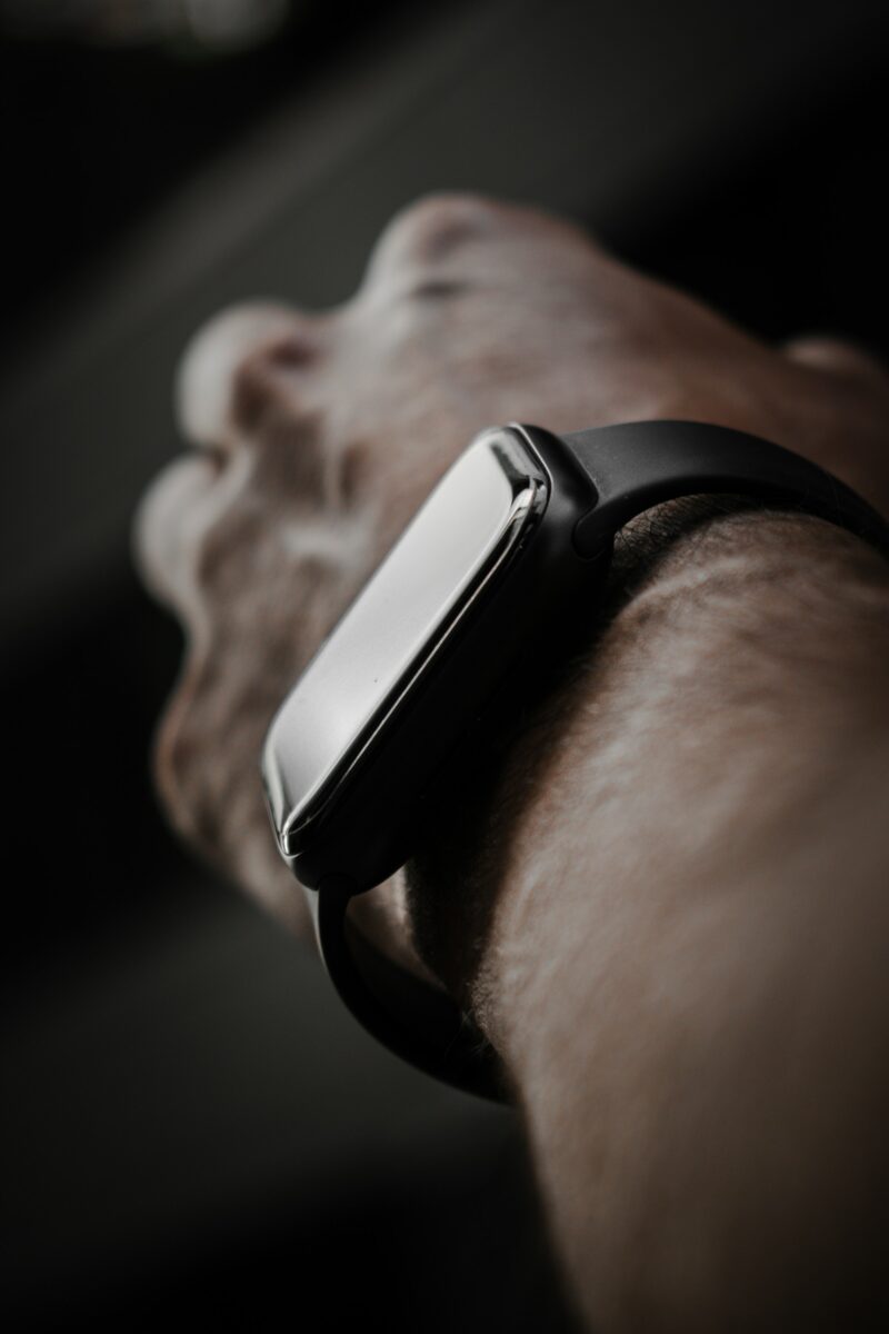 Close-up of a wrist wearing a black fitness watch with a dark screen against a dark background