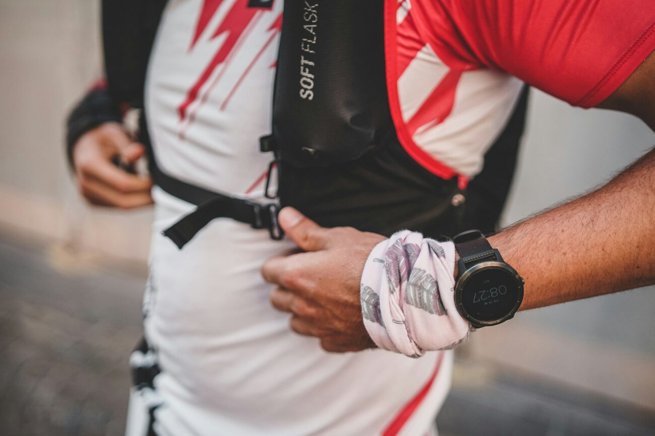 A runner in a hydration vest adjusting a strap, a sports watch on his wrist