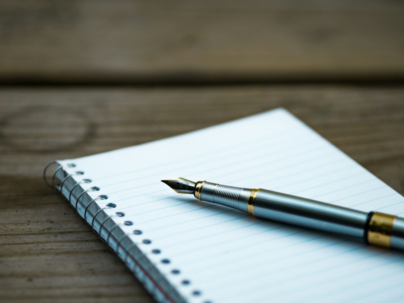 A fountain pen resting on a lined spiral notebook on a wooden table